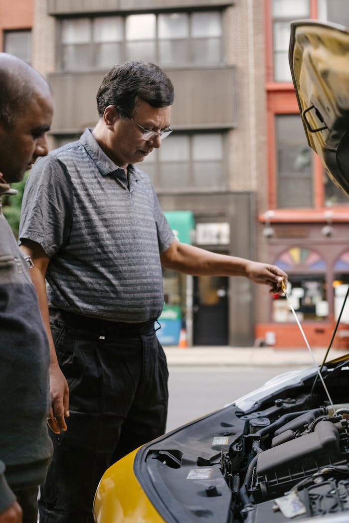 Two men inspecting a car engine on an urban street, focusing on maintenance.