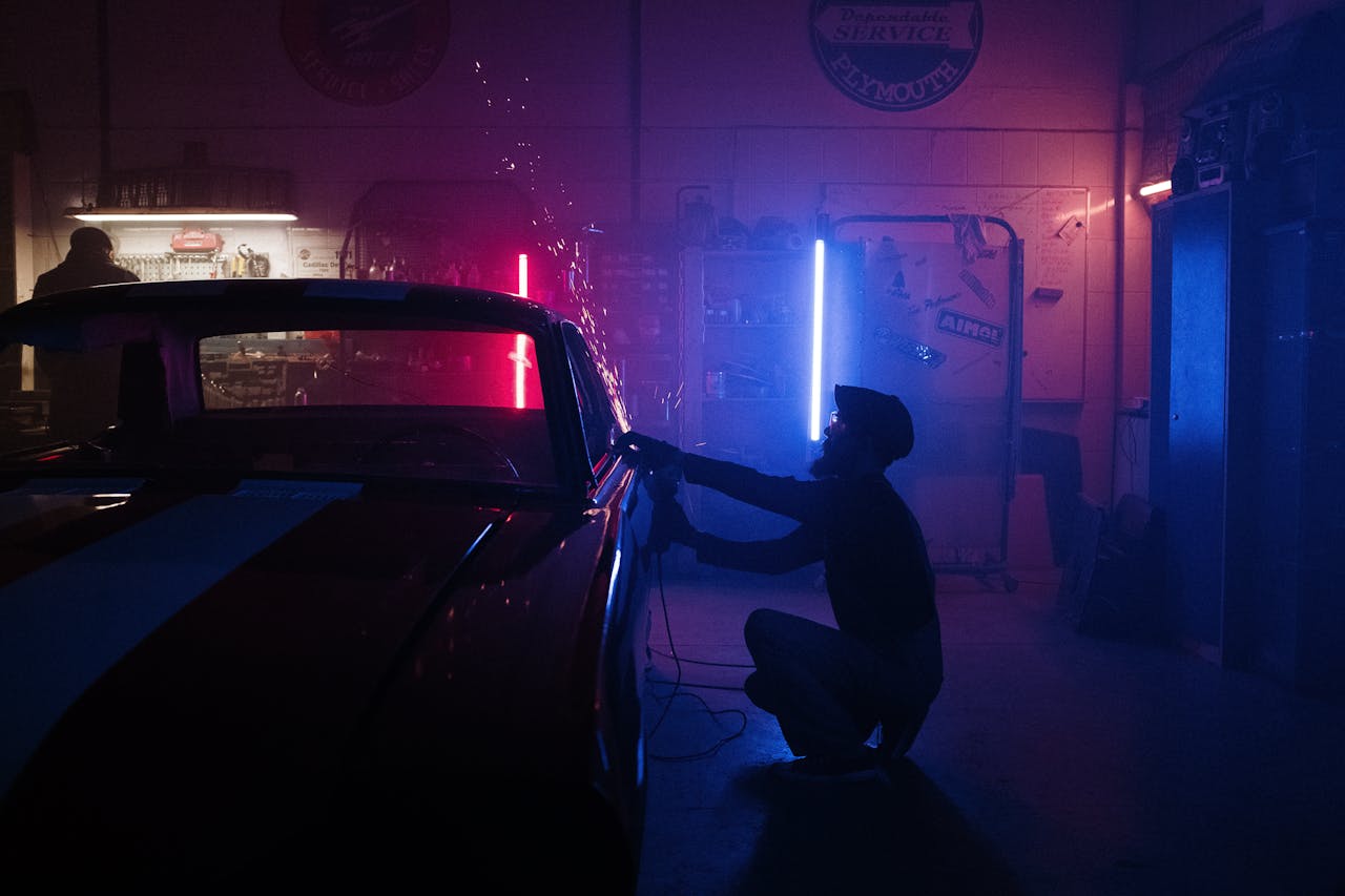 A mechanic works on a car in a neon-lit garage, creating a vibrant, moody atmosphere.