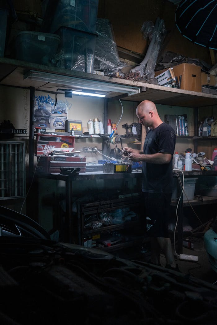 A mechanic diligently works on repairs in a dimly lit garage workshop, surrounded by tools.